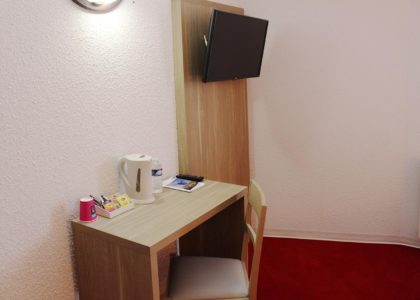Bureau avec télévision, bouilloire, et fournitures de bureau.
