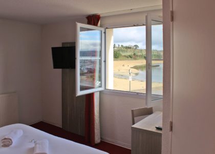 Vue sur plage depuis chambre d'hôtel lumineuse.